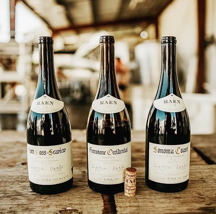 Drie flessen Pinot Noir van RAEN Winery – Fort Ross-Seaview, Freestone Occidental en Sonoma Coast – gepresenteerd op houten tafel in de wijnmakerij.